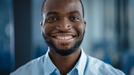 Téléchargez les photos : Fermer Portrait d'un Noir Afro-Américain bel homme en chemise décontractée bleu clair. Successful Man Calmly Sourit tout en regardant la caméra. Heureux homme d'affaires élégant ou un médecin à l'hôpital. - en image libre de droit