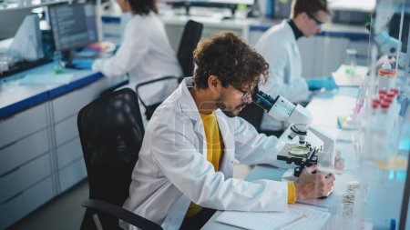 Photo for Medical Science Laboratory: Handsome Latin Scientist Looking Under Microscope to Analyse New Samples. Young Biotechnology Specialist, Using Advanced Equipment. - Royalty Free Image