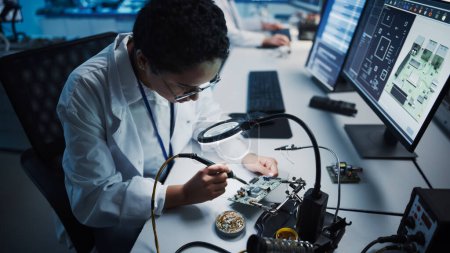 Photo for Modern Electronics Research, Development Facility: Black Female Engineer Does Computer Motherboard Soldering. Scientists Design Industrial PCB, Silicon Microchips, Semiconductors. High Angle Shot - Royalty Free Image