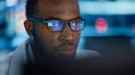 Photo for Portrait of Handsome Black Man Wearing Glasses Working Confidently on a Computer. Young Intelligent Male Engineer or Scientist Working in Laboratory. Bokeh Blue Background. Close-up Shot - Royalty Free Image