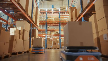 Foto de Future Technology 3D Concept: Automated Modern Retail Warehouse AGV Robots Transporting Cardboard Boxes in Distribution Logistics Center. Vehículos Guiados Automatizados Entregando Mercancías, Productos, Paquetes - Imagen libre de derechos
