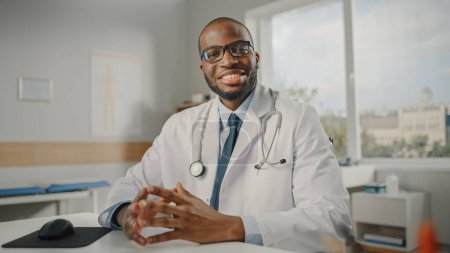 Téléchargez les photos : Fermer Portrait d'un médecin de famille afro-américain heureux portant des lunettes dans une clinique de santé. Réussi médecin noir en blouse blanche regarde la caméra et sourit dans le bureau de l'hôpital. - en image libre de droit