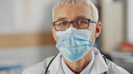 Photo for Close Up Portrait of a Senior Caucasian Male Doctor or Surgeon Wearing a Protective Face Mask and Glasses. Middle Aged Scientist Calmly Looking at Camera. Medical Care Specialist in Covid-19 Reality. - Royalty Free Image