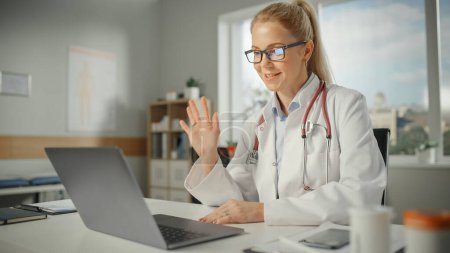 Photo for Doctor's Online Medical Consultation: Caucasian Female Physician is Making a Conference Video Call and Waving to a Patient on a Laptop Compute. Health Care Professional Explaining Test Results. - Royalty Free Image