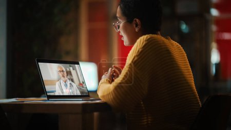 Téléchargez les photos : Belle femme latine multiethnique fait un appel vidéo à un médecin sur ordinateur portable dans un environnement créatif à la maison. Une spécialiste parle des résultats d'un test à une patiente devant une caméra en direct. - en image libre de droit