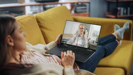 Photo for Beautiful Female Chatting in a Video Call with Her Female Family Doctor on Laptop from Living Room. Ill-Feeling Woman Making a Call from Home with Physician Over the Internet. - Royalty Free Image