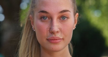 Photo for Close Up Portrait of Beautiful Young Woman Looking at Camera Neuterally with a Greenery Background. Blond Female Teenager Enjoying Fresh Air in the Park and Taking Care of her Wellbeing - Royalty Free Image