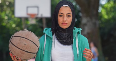 Téléchargez les photos : Portrait de belle jeune femme musulmane lançant un ballon de basket tout en regardant la caméra. Athlète féminine dans un hijab défiant les stéréotypes et suivant son rêve de devenir professionnelle - en image libre de droit