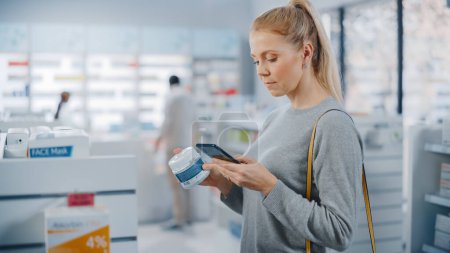 Photo for Pharmacy Drugstore: Portrait of a Beautiful Caucasian Woman Using Smartphone Search to Best Cream, Checks Jar for Eco Firendly Clean Ingredients and Proceeds to Checkout Counter With Happy Purchase - Royalty Free Image