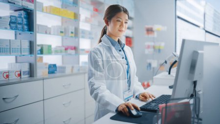 Photo for Pharmacy Drugstore: Beautiful Asian Pharmacist Uses Checkout Counter Computer, Does Inventory Checkup, Online Prescription of Medicine Packages, Drugs, Vitamin Boxes, Supplements, Health Care Products - Royalty Free Image