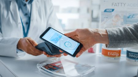 Photo for Pharmacy Drugstore Checkout Cashier Counter: Pharmacist and a Customer Using NFC Smartphone with Contactless Payment Terminal to Buy Prescription Medicine, Health Care Goods. Close-up Shot - Royalty Free Image
