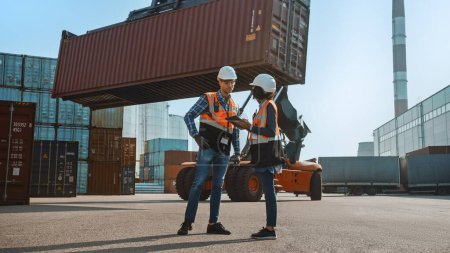 Photo for Multiethnic Female Industrial Engineer with Tablet Computer and Male Foreman Worker in Hard Hats and Orange High-Visibility Vests Stand in Container Terminal. Colleagues Talk About Logistics Business. - Royalty Free Image