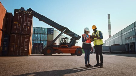 Photo for Multiethnic Female Industrial Engineer with Tablet and Black African American Male Supervisor in Hard Hats and Safety Vests Stand in Container Terminal. Colleagues Talk About Logistics Operations. - Royalty Free Image