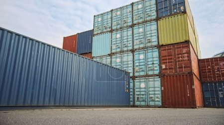 Téléchargez les photos : Prise de vue à faible angle d'un terminal industriel situé dans un centre d'opérations logistiques d'un chantier naval avec des conteneurs de fret en acier rouge et bleu. Nuageux en plein air. - en image libre de droit