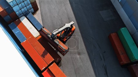 Photo for Aerial Top Down Shot of a Container Handler Carrying a Large Red Cargo Container in a Shipyard Terminal. Driver of the Machine is Loading the Crate in the Logistics Center Depot. - Royalty Free Image