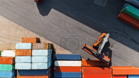 Téléchargez les photos : Vue aérienne du haut vers le bas d'un conteneur transportant un grand conteneur de fret rouge dans un terminal de chantier naval. Le conducteur de la machine charge la caisse dans le dépôt du centre logistique. - en image libre de droit