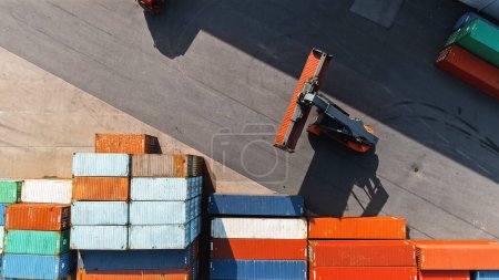 Foto de Aerial Top Down Shot of a Container Handler Carrying a Large Red Cargo Container in a Shipyard Terminal. El conductor de la máquina está cargando la caja en el almacén del centro de logística. - Imagen libre de derechos