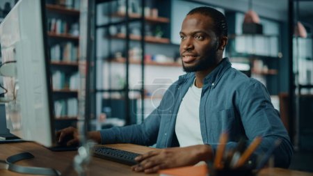 Photo for Handsome Black African American Specialist Working on Desktop Computer in Creative Home Living Room. Freelance Male is Working on a Finance Presentation Report for Clients and Employer. - Royalty Free Image