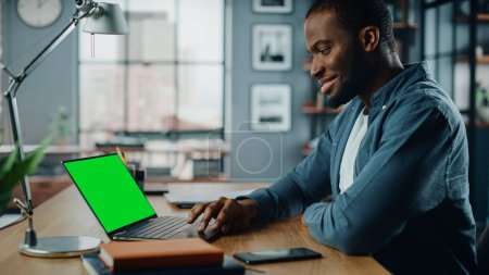 Photo for Handsome Black African American Specialist Working on Laptop Computer with Green Screen Mock Up Display at Home Living Room. Freelance Man Chatting to Clients Over the Internet on Social Networks. - Royalty Free Image