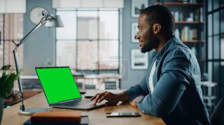 Photo for Handsome Black African American Specialist Working on Laptop Computer with Green Screen Mock Up Display at Home Living Room. Freelance Man Chatting to Clients Over the Internet on Social Networks. - Royalty Free Image