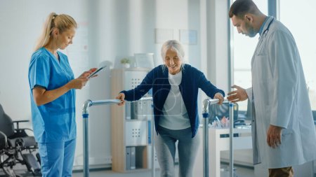 Photo for Hospital Physical Therapy: Portrait of Strong Senior Female Patient with Injury Successfully Walks Holding Parallel Bars. Physiotherapist, Rehabilitation Doctor, Help, Assist Disabled Patient - Royalty Free Image