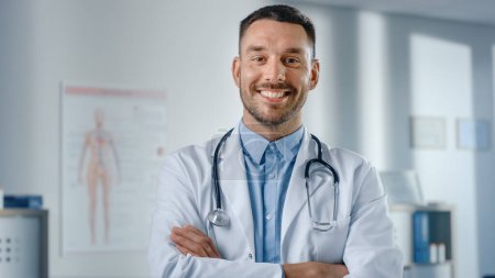 Photo for Portrait of Handsome Caucasian Medical Doctor Wearing White Coat and Stethoscope Crosses Arms, Standing in His Health Clinic Office. Successful, Confident Physician Looks at the Camera, Smiles - Royalty Free Image