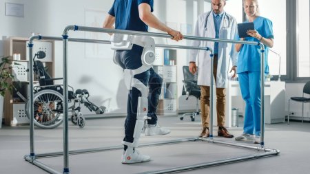Photo for Modern Hospital Physical Therapy: Patient with Injury Walks Wearing Advanced Robotic Exoskeleton. Physiotherapy Rehabilitation Scientists, Engineers use Tablet Computer to Help Disabled Person - Royalty Free Image