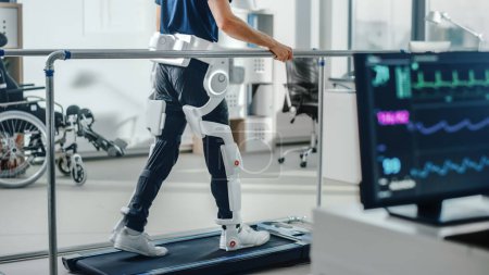 Photo for Modern Hospital Physical Therapy: Patient with Injury Walks on Treadmill Wearing Advanced Robotic Exoskeleton Legs. Physiotherapy Rehabilitation Technology to Make Disabled Person Walk. Focus on Legs - Royalty Free Image