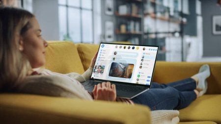 Photo for Beautiful Caucasian Female is Using Laptop for Chatting with Fiends in Social Network at Home Living Room while Lying on a Couch Sofa. Social Media Marketer Working From Home, Surfing the Internet. - Royalty Free Image