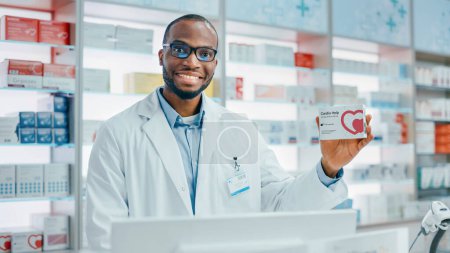 Photo for Pharmacy Drugstore: Portrait of Professional Black Male Pharmacist Holding Package of Heart Medications, Looking at Camera, Smiling. Specialist Recommending Best Product - Royalty Free Image