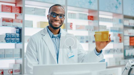 Téléchargez les photos : Pharmacie Drugstore : Portrait of Professional Black Male Pharmacist Holding Package of Vitamins, Looking at Camera, Smiling. Spécialiste recommandant le meilleur produit - en image libre de droit