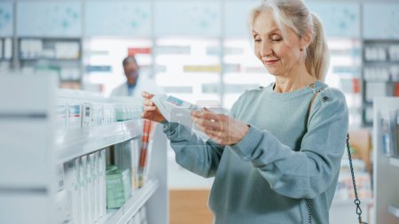 Téléchargez les photos : Pharmacie Drugstore : Belle femme âgée marchant entre les allées et les étagères avec médecine, Choisir d'acheter des médicaments, médicaments, vitamines, produits de soins de santé, suppléments avec un design d'emballage moderne - en image libre de droit