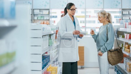 Téléchargez les photos : Pharmacie : Un pharmacien professionnel aide une belle cliente âgée avec des recommandations, des conseils et des discussions en médecine. Droguerie avec plein de médicaments, pilules, soins de santé, emballages de produits de beauté - en image libre de droit