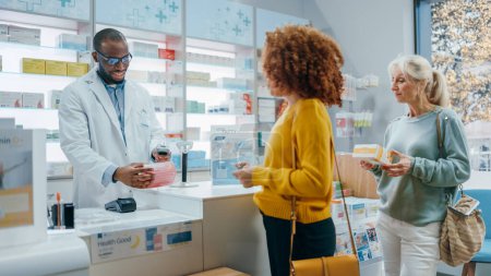 Foto de Pharmacy Drugstore Checkout Counter: Professional Black Pharmacist Proporciona el mejor servicio al cliente a diversos grupos de clientes multiétnicos que compran medicamentos pagando con tarjetas de crédito de pago sin contacto - Imagen libre de derechos