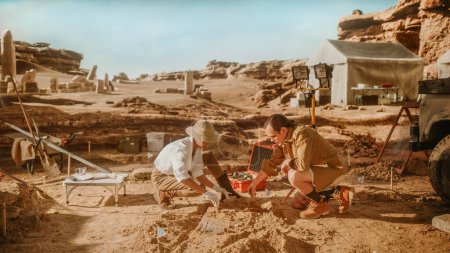 Foto de Sitio de excavación arqueológica: Dos grandes arqueólogos trabajan en el sitio de excavación, limpiando cuidadosamente con cepillos y herramientas artefactos culturales de civilización antigua recién descubiertos, restos fósiles - Imagen libre de derechos