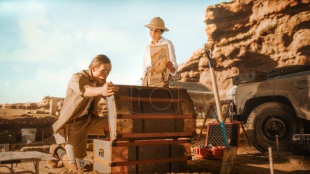 Photo for Archaeological Digging Site: Two Great Adventurers on Treasure Hunt Talk and work with Opened Chest with Unspeakable Treasures. Ancient Civilization Hidden Gold Found - Royalty Free Image