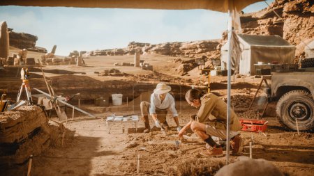 Foto de Sitio de excavación arqueológica: Dos grandes arqueólogos trabajan en el sitio de excavación, limpiando cuidadosamente con cepillos y herramientas artefactos culturales de civilización antigua recién descubiertos, restos fósiles - Imagen libre de derechos