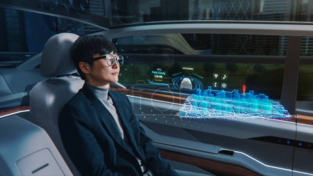 Téléchargez les photos : Concept futuriste : l'homme d'affaires élégant définit l'emplacement sur une application interactive de navigation 3D sur un tableau de bord de réalité augmentée tout en étant assis dans une voiture électrique autonome zéro émission. - en image libre de droit