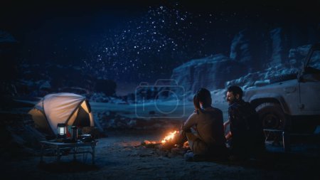 Téléchargez les photos : Femme voyageuse assise sur son capot de VUS hors route regardant le ciel nocturne pendant qu'elle campait dans le canyon près d'un feu de camp. Une femme voyageuse aventurière en voyage inspirant s'émerveille devant les étoiles de la Voie lactée - en image libre de droit