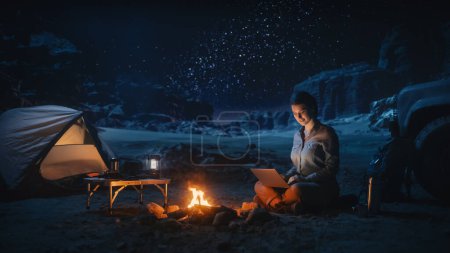 Téléchargez les photos : Femme voyageuse assise sur son capot de VUS hors route regardant le ciel nocturne pendant qu'elle campait dans le canyon près d'un feu de camp. Une femme voyageuse aventurière en voyage inspirant s'émerveille devant les étoiles de la Voie lactée - en image libre de droit