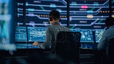 Photo for Professional IT Technical Support Specialist and Software Developer Working on Computer in Monitoring Control Room with Digital Screens. Employee Use Headphones with Mic and Talking on a Call. - Royalty Free Image