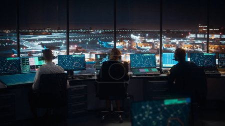 Diverse Fluglotsen arbeiten nachts in einem modernen Flughafen-Tower. Bürozimmer ist voll von Desktop-Computer-Displays mit Navigationsbildschirmen, Flugdaten für Fluglotsen.