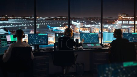 Photo for Diverse Air Traffic Control Team Working in Modern Airport Tower at Night. Office Room Full of Desktop Computer Displays with Navigation Screens, Airplane Departure and Arrival Data for Controllers. - Royalty Free Image