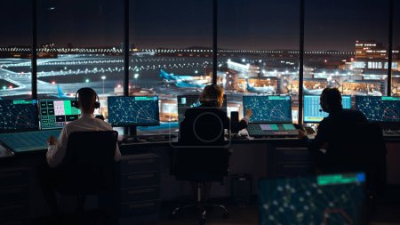 Foto de Equipo de Control de Tráfico Aéreo Diverso Trabajando en la Torre Moderna del Aeropuerto por la Noche. Sala de oficina llena de pantallas de computadora de escritorio con pantallas de navegación, datos de salida y llegada de aviones para controladores. - Imagen libre de derechos