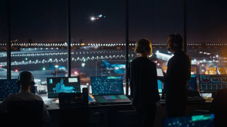 Foto de Controladores de tráfico aéreo femeninos y masculinos con auriculares Hablan en la torre del aeropuerto por la noche. Sala de oficina llena de pantallas de computadora de escritorio con pantallas de navegación, datos de radar de vuelo de avión para controladores. - Imagen libre de derechos