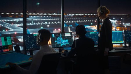 Foto de Controladores de tráfico aéreo femeninos y masculinos con auriculares Hablan en la torre del aeropuerto por la noche. Sala de oficina llena de pantallas de computadora de escritorio con pantallas de navegación, datos de radar de vuelo de avión para controladores. - Imagen libre de derechos