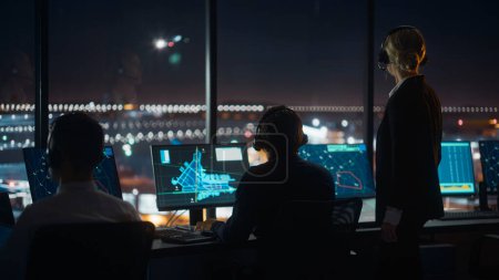 Photo for Female and Male Air Traffic Controllers with Headsets Talk in Airport Tower at Night. Office Room Full of Desktop Computer Displays with Navigation Screens, Airplane Flight Radar Data for Controllers. - Royalty Free Image