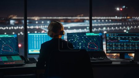 Photo for Female Air Traffic Controller with Headset Talk on a Call in Airport Tower at Night. Office Room is Full of Desktop Computer Displays with Navigation Screens, Airplane Flight Radar Data for the Team. - Royalty Free Image