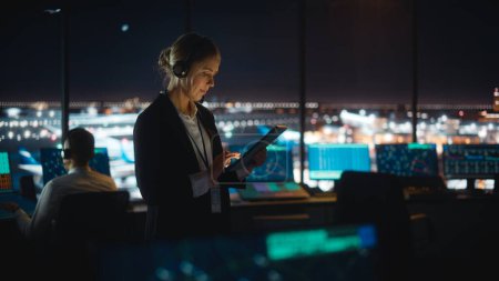 Foto de Controlador de tráfico aéreo femenino caucásico que trabaja en la tableta en la torre del aeropuerto. La sala de oficina está llena de pantallas de computadora de escritorio con pantallas de navegación, datos de radar de vuelo de avión para el equipo. - Imagen libre de derechos