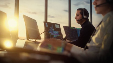 Photo for Male Air Traffic Controller with Headset Talk on a Call in Airport Tower. Office Room is Full of Desktop Computer Displays with Navigation Screens, Airplane Departure and Arrival Data for the Team. - Royalty Free Image